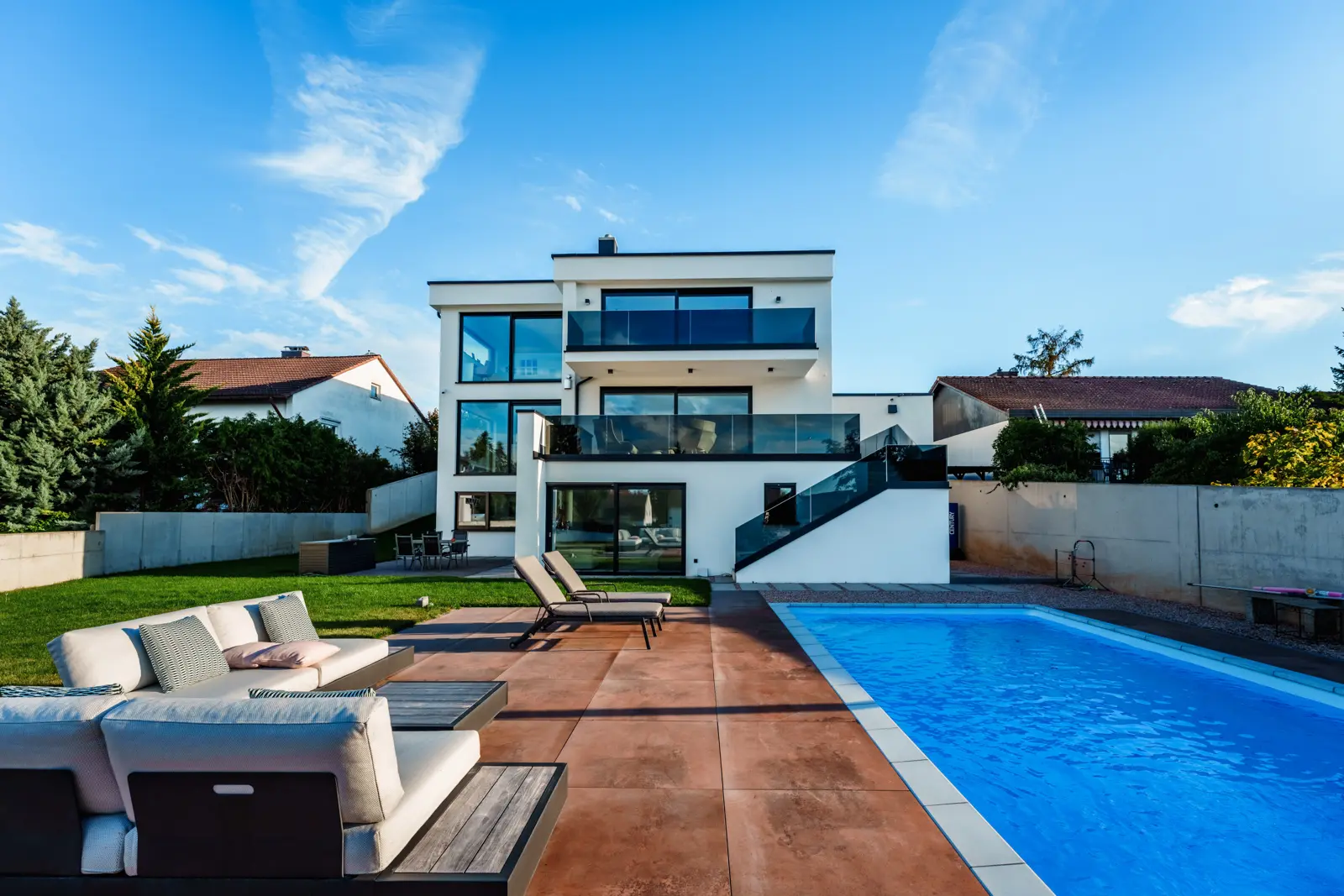Modernes mehrstöckiges Haus mit Pool im Garten, Terrassenmöbeln und Sonnenliegen.